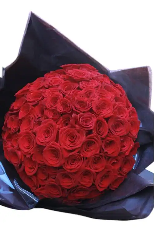 A large bouquet of vibrant red roses from a flower shop Manhattan NYC, wrapped in dark paper and arranged in a dense cluster with lush, velvety petals, set against a plain white background.