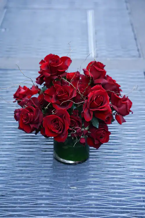 A bouquet of vibrant red roses arranged in a glass vase, placed on a patterned gray metallic surface&mdash;perfect for anyone seeking flowers for sale Manhattan NYC.